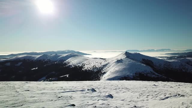 在Amerinkogel地区，一架无人机拍摄到被雪覆盖的阿尔卑斯山。山谷里有浓雾。山坡上茂密的森林。奥地利阿尔卑斯山的冬天。无尽的山脉。阳光明媚的一天。视频素材