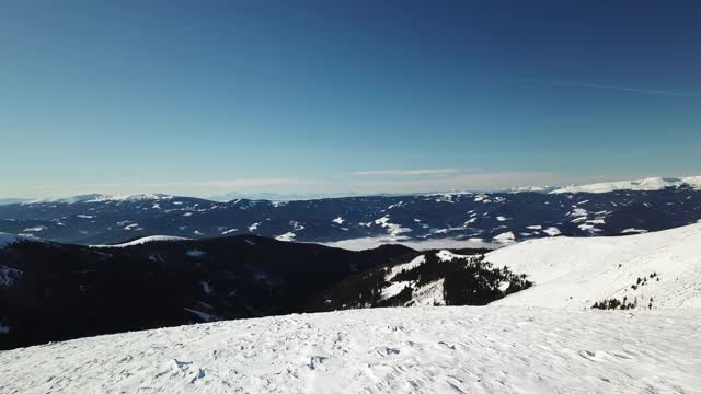 在Amerinkogel地区，一架无人机拍摄到被雪覆盖的阿尔卑斯山。山谷里有浓雾。山坡上茂密的森林。奥地利阿尔卑斯山的冬天。无尽的山脉。阳光明媚的一天。视频素材