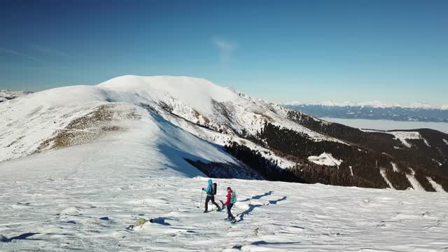 无人机拍摄到一对夫妇穿着雪地鞋徒步前往Amerinkogel峰。奥地利阿尔卑斯山的冬天。无尽的山脉，覆盖着粉状的雪。山谷里有浓雾。户外活动视频素材