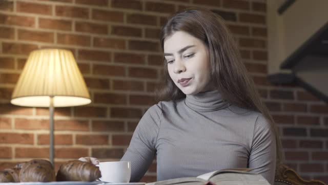 漂亮的黑发白种女人一边喝茶或咖啡一边思考。美丽自信的富家女在家吃早餐的肖像。奢侈和生活方式的概念。视频素材