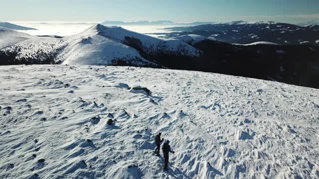 无人机拍摄到一对夫妇穿着雪地鞋徒步前往Amerinkogel峰。奥地利阿尔卑斯山的冬天。无尽的山脉，覆盖着粉状的雪。山谷里有浓雾。户外活动视频素材