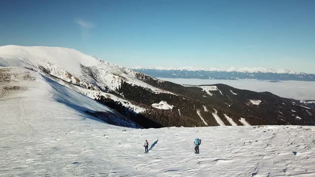 无人机拍摄到一对夫妇穿着雪地鞋徒步前往Amerinkogel峰。奥地利阿尔卑斯山的冬天。无尽的山脉，覆盖着粉状的雪。山谷里有浓雾。户外活动视频素材