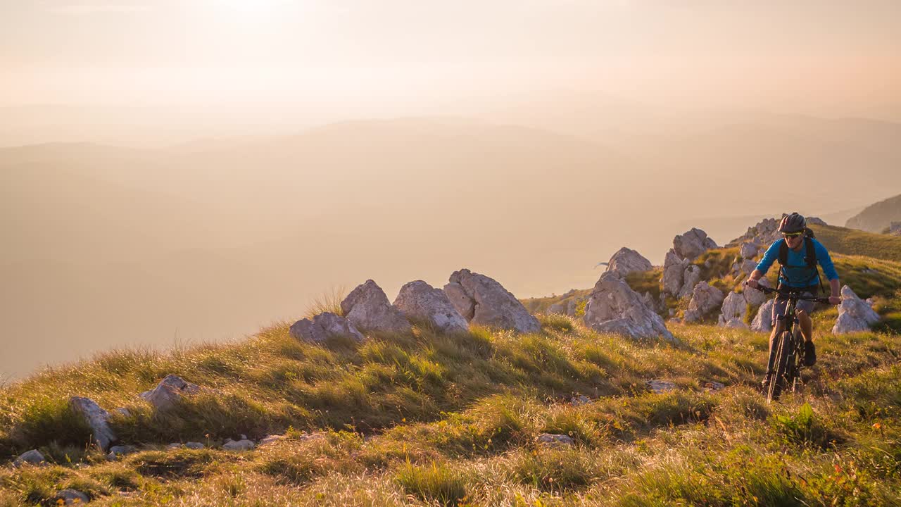 在大自然中做户外运动，骑山地自行车上山，在日落时被绿色的草地和山脉包围视频素材