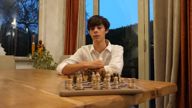 在一盘国际象棋中，专注的男孩在棋盘上移动一个卒子视频素材