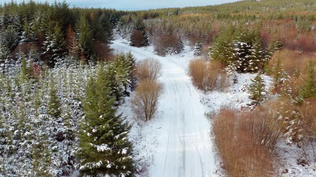 在苏格兰西南部的邓弗里斯和加洛韦，这是一架无人机在一条被雪覆盖的乡村道路上向后流动的画面视频素材