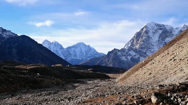 在阳光明媚的早晨，人们在雄伟的Khubu冰川的岩石冰碛中徒步旅行，靠近Lobuche，尼泊尔的喜马拉雅山脉和崎岖的积雪覆盖的山脉。视频素材