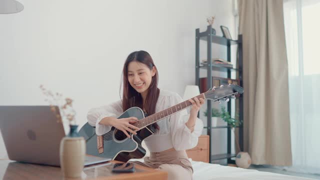 快乐的年轻女子集中学习吉他使用笔记本电脑坐在家里的客厅视频素材