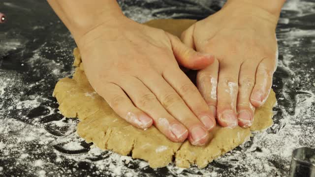 女性用手擀生姜饼，特写。女人正在黑色的木桌上用手揉平面团。厨师在现代厨房里用擀面杖擀面团视频素材