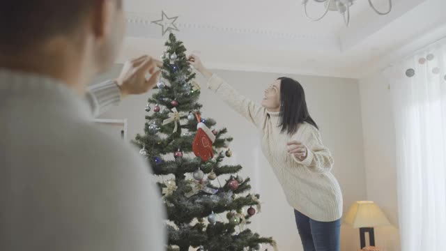 积极的白人妇女在家里装饰圣诞树与模糊的男子与妻子在前面交谈。快乐的女士在享受除夕装饰房子的肖像视频素材