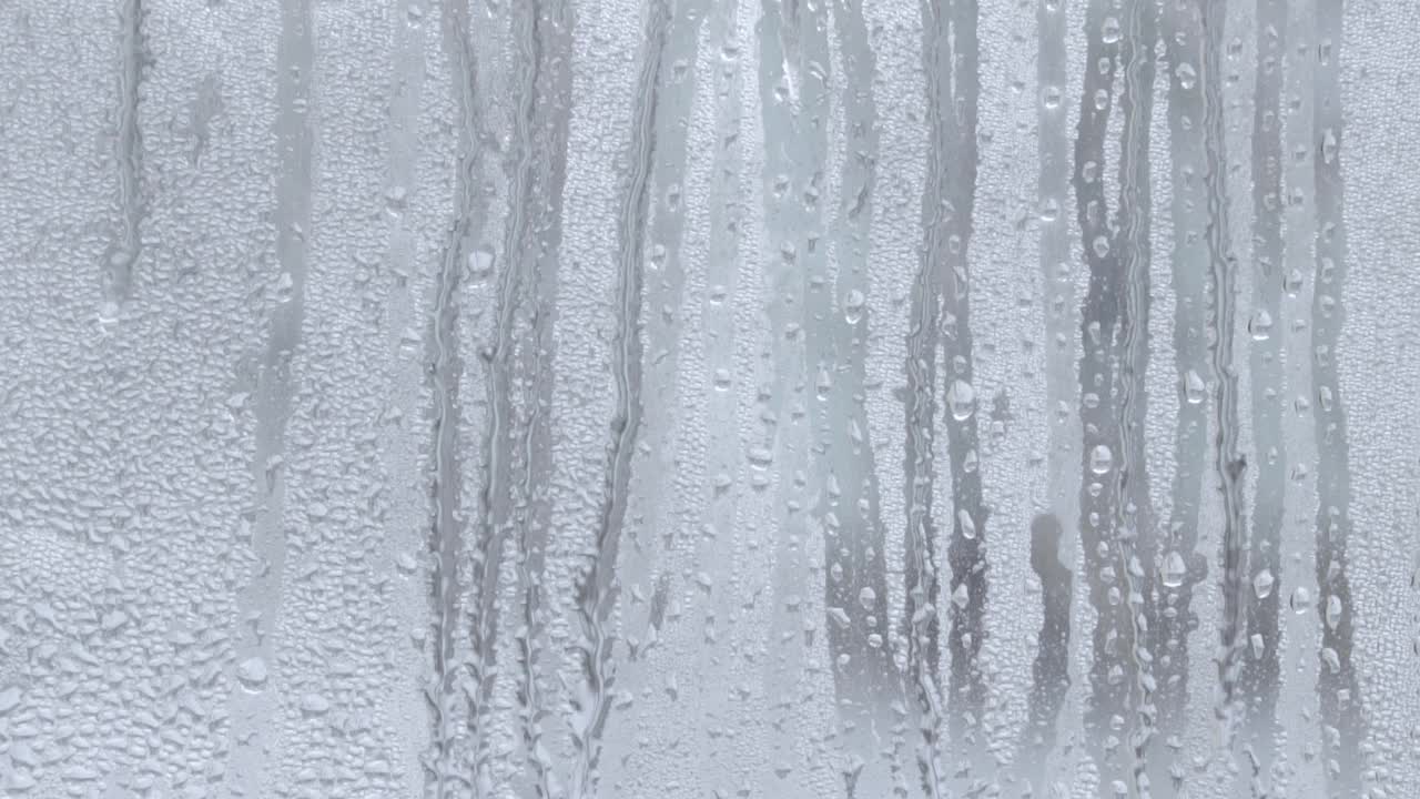 水滴飞溅到玻璃上。雨天的窗户。用大滴的水或雨浸湿玻璃杯。在大雨期间水滴在一个清晰的玻璃表面的视频。滴水视频素材