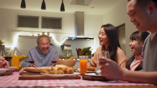 幸福的家庭时间和关系，亚洲大家庭有一个小聚会，一起在家里吃东西。爷爷很高兴看到他的孩子和侄子在家里的餐桌上吃饭，分享食物。视频素材