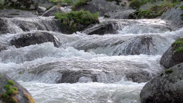 山间的河水在冒泡。水如瀑布般流过岩石，轻轻地将它们包围。石头上有绿色植物和苔藓。水流向观赏者移动，水流结构清晰可见。视频素材