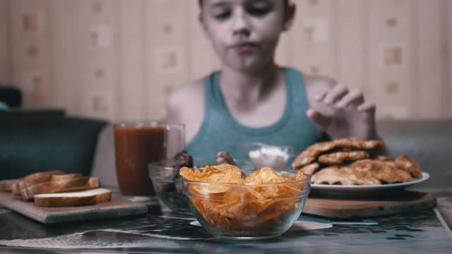 饥饿的小手从盘子里拿起脆脆的金色薯片。晚餐中的垃圾食品视频素材