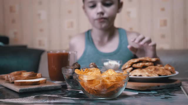 饥饿的小手从盘子里拿起脆脆的金色薯片。晚餐中的垃圾食品视频素材