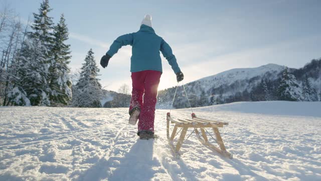 低角度:当女人拉着雪橇在白雪覆盖的草地上奔跑时，雪花在空中飞舞。视频素材