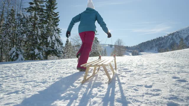 低角度:一个陌生的年轻女子拉着她的雪橇在白雪覆盖的草地上奔跑视频素材