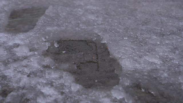 近距离观察:浅蓝色的医用口罩落在雪水里的一个脚印里。视频素材