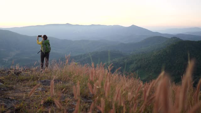 女性旅行者徒步登山，用智能手机拍照视频素材