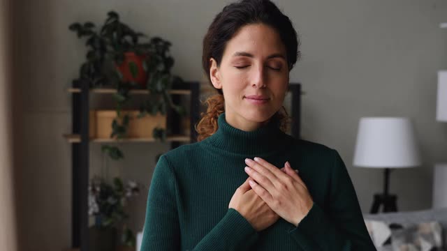 美丽真诚的女人站在室内，双手合十放在心上视频素材