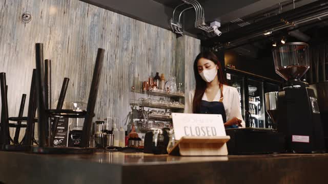 企业主迷人的年轻夫妇女人在围裙挂我们是开放的标志在前门欢迎客户到新咖啡馆。快乐的服务员戴着保护面罩，在咖啡馆拿着开放的标志。视频素材