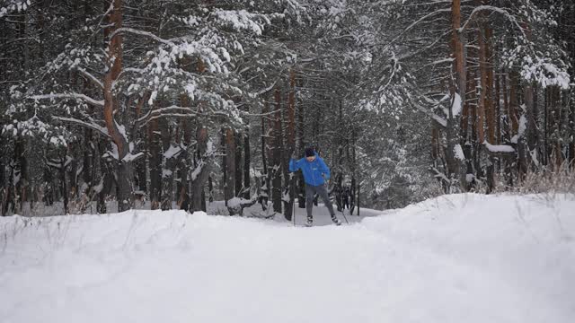 一个年轻人正在冬季森林里进行越野滑雪。运动员滑冰。视频素材