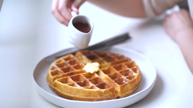 一个女人正在把糖浆倒在加了糖的华夫饼上视频素材