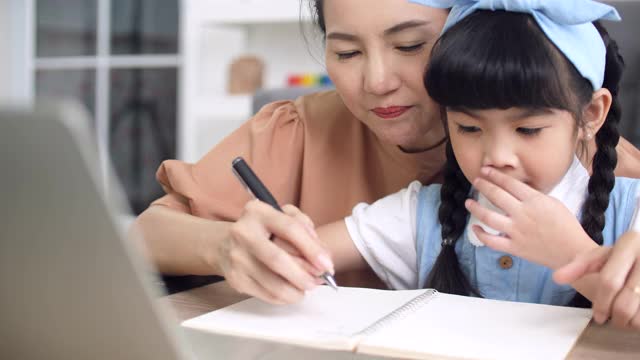 年轻的母亲教女儿在家用笔记本电脑做作业视频素材