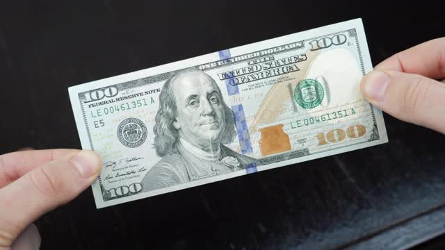 一个人手里拿着一百美元的钞票。金融业务的概念。纸币，现金货币。世界经济的概念视频素材