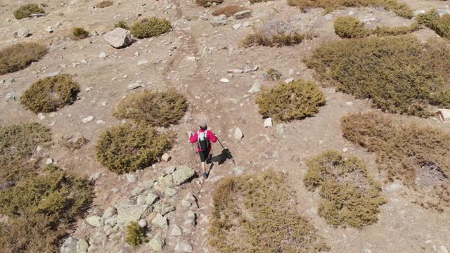 一个男人的鸟瞰图在帽子和短裤和一个背包与徒步杆子沿着高山山谷视频素材