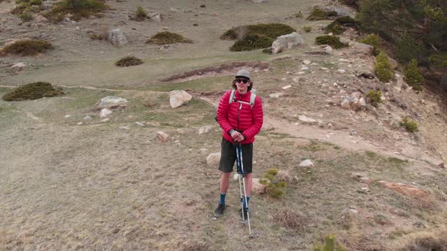 一个男人的鸟瞰图在帽子和短裤和一个背包与徒步杆子沿着高山山谷视频素材