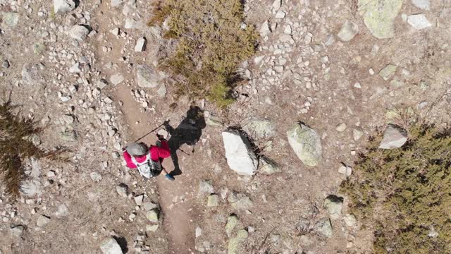 一个男人的鸟瞰图在帽子和短裤和一个背包与徒步杆子沿着高山山谷视频素材