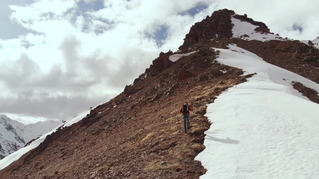 登山者在石头和雪的交界处的山脊上，背着背包和拐杖爬上山坡。北高加索山脉高处鸟瞰图视频素材