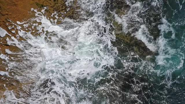 碧绿的海水在岩石海岸上波涛起伏。航拍慢动作视频。视频素材