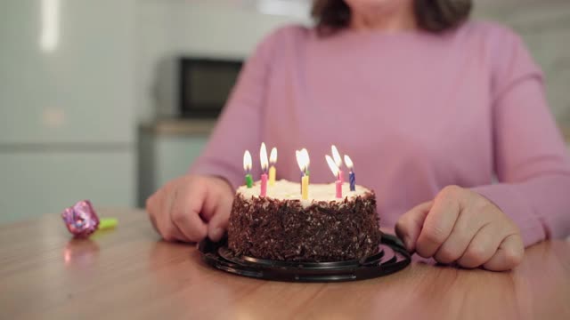 女人吹灭生日蛋糕上的蜡烛，坐在桌子旁，庆祝视频素材