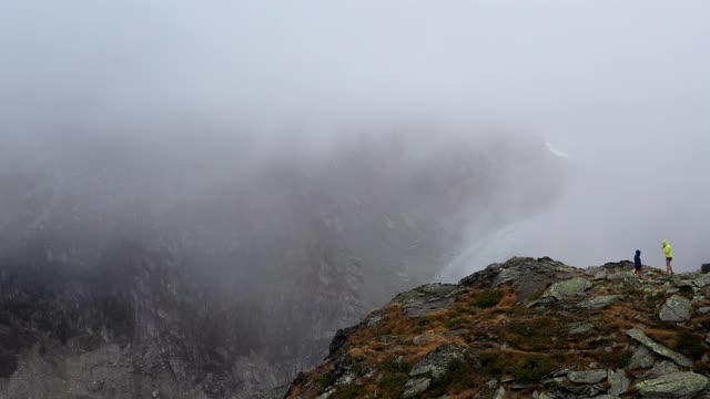 无人机拍摄的两名跑步者跑上一座俯瞰山谷的山的边缘视频素材