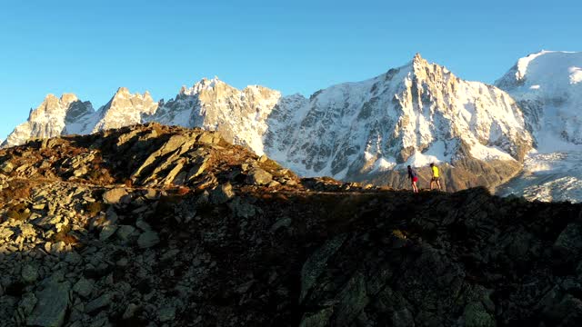 无人机拍摄的两个跑步者沿着山的边缘跑，在山顶停下来视频素材