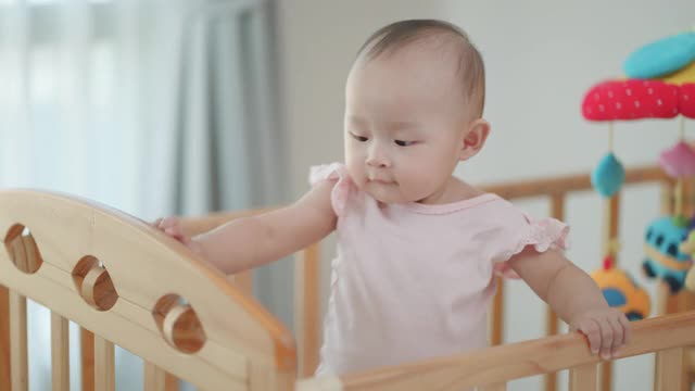 可爱的笑亚洲婴儿女孩站在一个木制的圆床上学习站在她的婴儿床在卧室在家里。视频素材