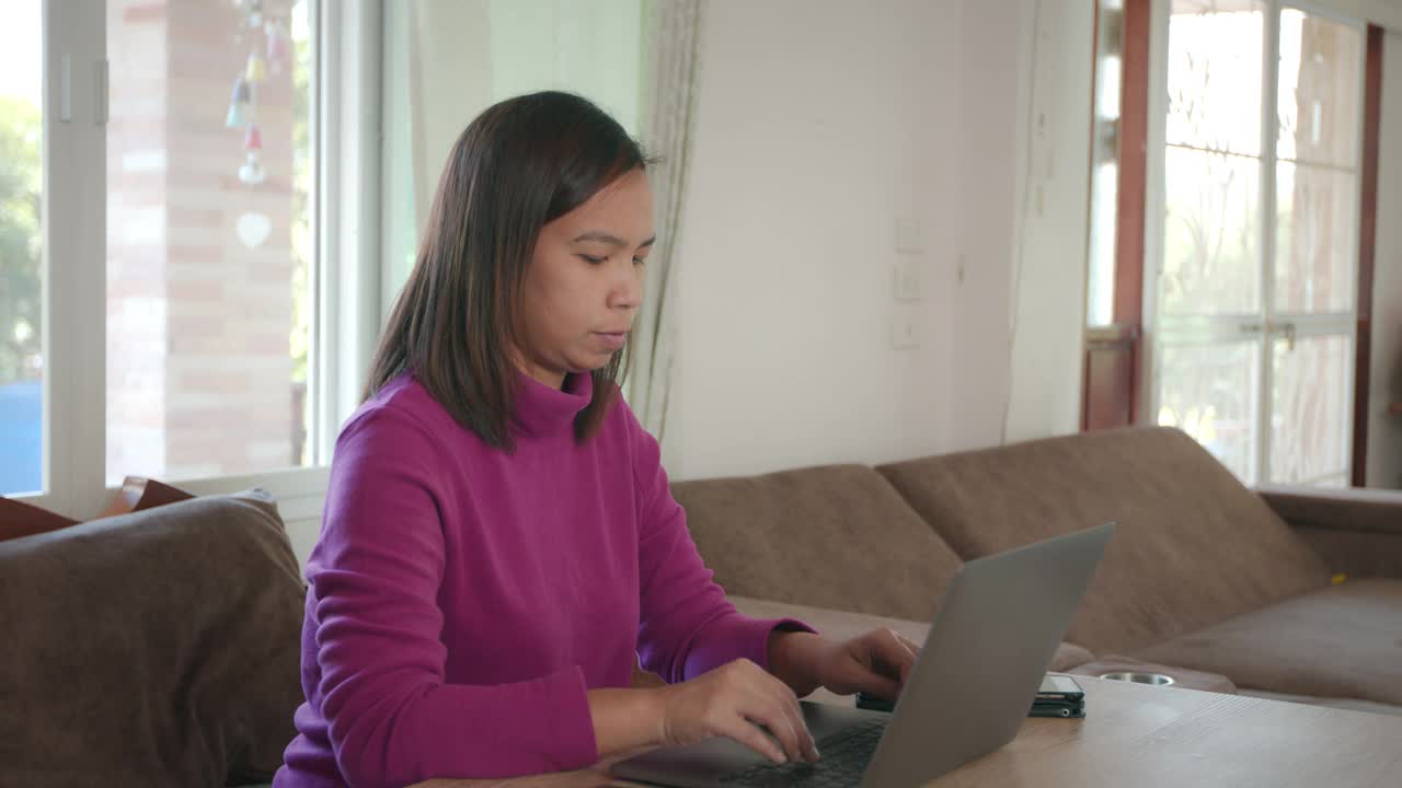 年轻的亚洲女人是打字数据笔记本电脑和思考与成功，而工作在家里。在家工作的女性员工。视频素材