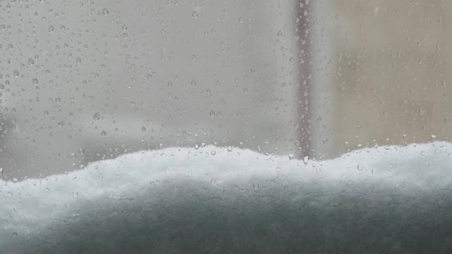 一扇窗户上的雨滴和飘落的雪花视频下载