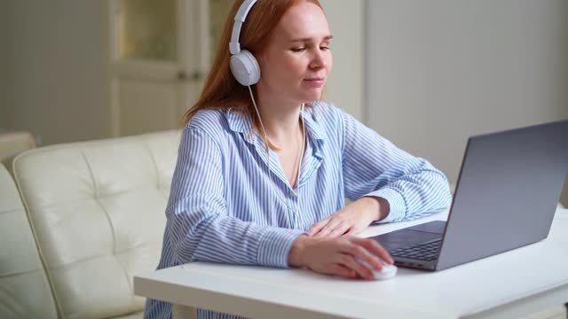 一位戴着耳机的女士在家里通过笔记本电脑开始了一节课或网络研讨会。视频素材