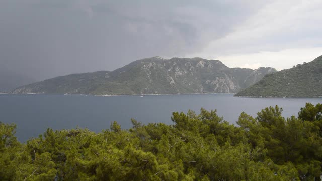 一场带着雨、雷暴和闪电的暴风雨正在地中海沿岸逼近，土耳其马尔马里斯镇附近的山区被森林覆盖。视频加速拍摄视频下载