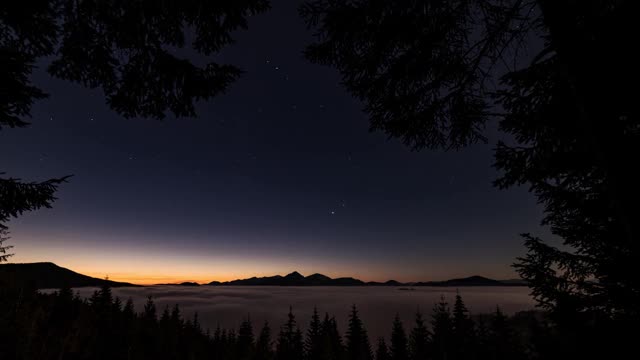 清晨在神奇的森林与星星在蓝色的天空，雾云在山谷和美丽的颜色日出前在野生自然景观时间流逝视频素材