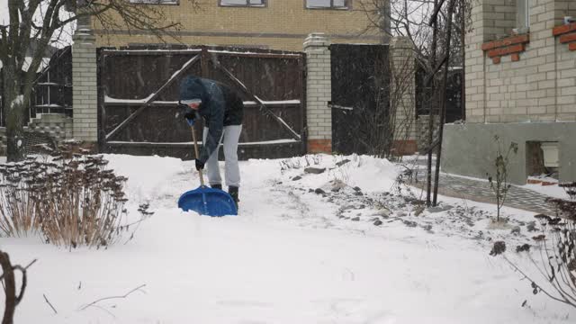 降雪。年轻人用铲子清除积雪。工人在冬季暴风雪清扫后院的雪视频素材