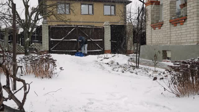 年轻人正在用铁锹铲雪。男性正在铲雪的道路附近的房子在冬天视频素材