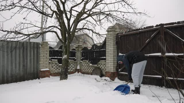 人们正在清理暴风雪中的道路。降雪。一名男子在后院的篱笆旁用铲子清理积雪视频素材