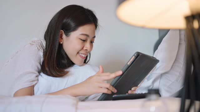 亚洲开朗的大学女性阅读从didital平板电脑准备期末考试在线学习教育在家自学在卧室视频素材