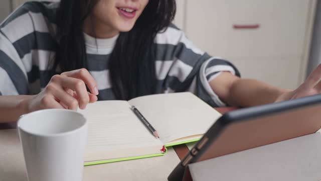 年轻的亚洲女孩学习在线在线学习课程，家庭学校写在笔记本上，集中精力做家庭作业，远程教育，家庭学校，在禁闭期间在家工作视频素材