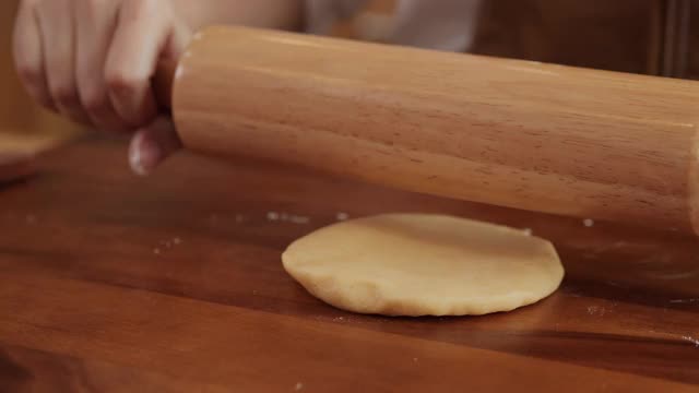 在家庭厨房里，厨师在木桌上用擀面杖揉生面团做饼干。视频素材