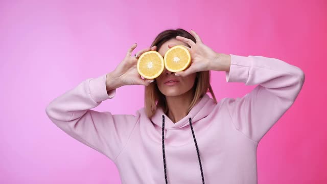 穿着休闲粉色衣服的女人拿着橘子跳舞视频素材