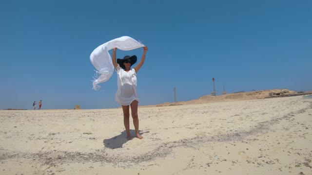 夏天无忧无虑的女人在海滩上拿着围巾织物在风中慢镜头摇摆。吉敦岛天堂海滩在赫尔加达，埃及视频素材